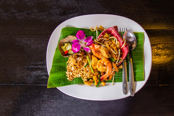 泰国炸面条垫泰国与虾和蔬菜的白色陶瓷菜装饰与兰花把黑暗木表格选择焦点