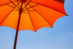 橙色颜色海滩伞使木为受保护的阳光与明亮的蓝色的天空背景