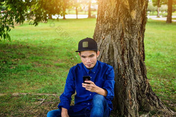 男人。蓝色的衬衫是使用智能手机互联网在线技术社会媒体到处都是和自然背景阳光