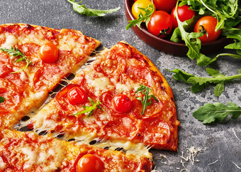 片意大利辣香肠披萨与樱桃西红柿切片美味的意大利辣香肠披萨的灰色石头背景