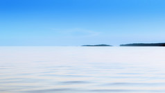 很酷的自然运动模糊背景白色光滑的波的水表面和远程轮廓的岛屿的地平线下的蓝色的天空模糊健美的过滤器空间为复制