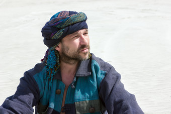 肖像深思熟虑的成熟的有胡子的男人。他的头巾与背景白色桑迪沙漠肖像男人。他的头巾对的背景的检查
