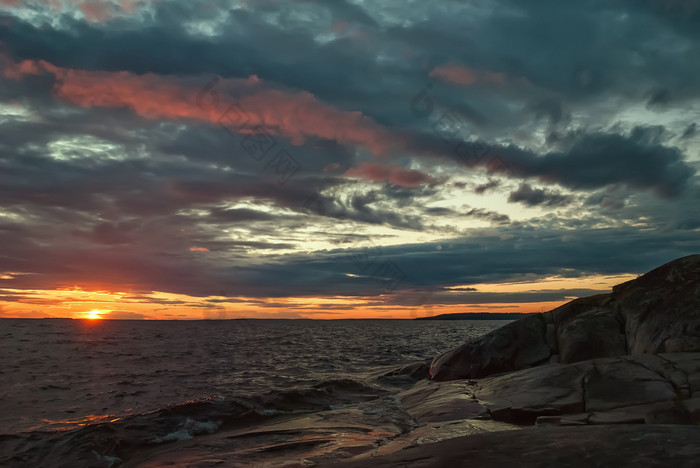 日落的多云的天空在石头海滨之前风暴晚上景观之前的风暴海