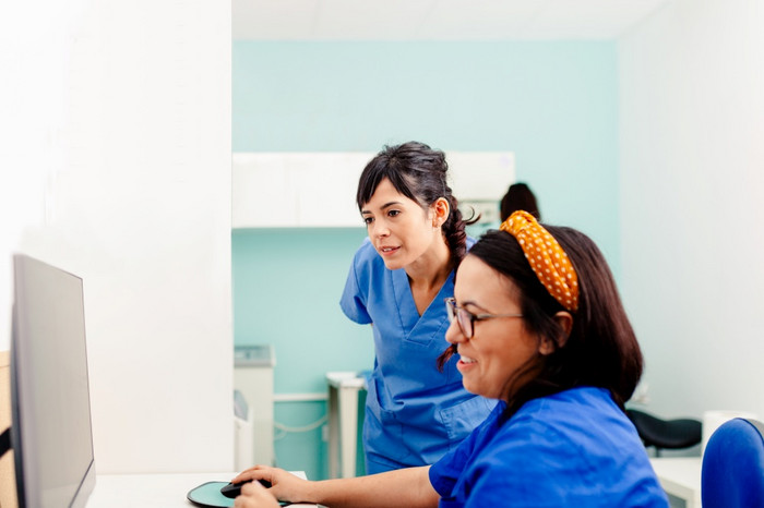 两个护士使用电脑x射线房间一个他们穿眼镜和坐着附近的桌子上两个护士使用电脑x射线房间