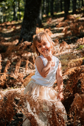 肖像小高加索人婴儿女孩的森林在蕨类植物看走了小高加索人婴儿女孩蹲的森林在蕨类植物