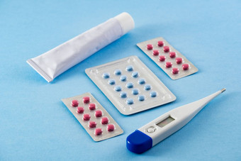 泡包蓝色的和粉红色的药片白色药膏管和电子数字温度计蓝色的背景:医疗保健和医疗概念