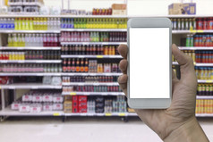 手持有智能手机与白色空白屏幕在模糊超市和零售商店购物购物中心室内背景为产品显示蒙太奇