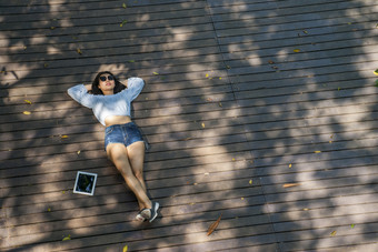 的蓝色的衬衫女人坐着看的文本的平板电脑而坐着的公园从高角
