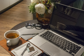 白色茶杯木桌子上与玫瑰花瓶放置开放的移动PC和工作的生活房间首页