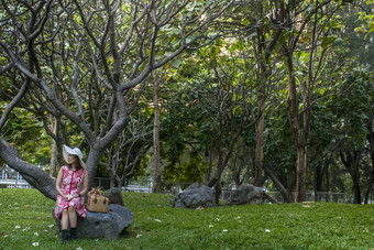 美丽的女孩红色的衣服坐着岩石下树的花园