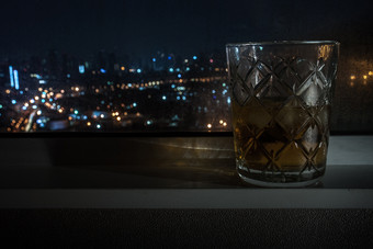 的威士忌玻璃放置旁边的窗口的酒店房间的城市与外视图散景光从的车头灯合适的为使背景图片为广告