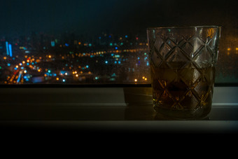 的威士忌玻璃放置旁边的窗口的酒店房间的城市与外视图散景光从的车头灯合适的为使背景图片为广告