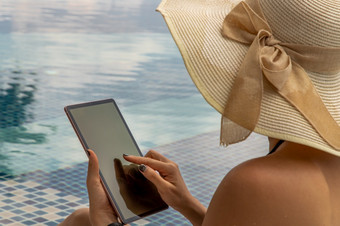 假期生活方式场景年轻的女人黑色的比基尼使用平板电脑而坐着的池早....时间周末和假期生活方式放松的在游泳池边