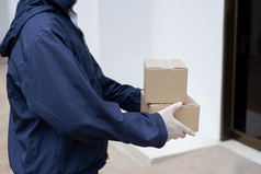 包裹交付概念的邮递员白色橡胶手套和光重量黑暗蓝色的外套等待手小包裹他的客户端前面的建筑