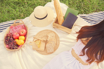 野餐概念的回来的少女与长棕色（的）头发的舒适的白色衣服说谎下来的野餐布和阅读书
