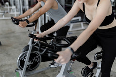 锻炼概念的两个体育运动俱乐部参与者玩锻炼自行车机为做他们的有氧运动旁边每一个其他