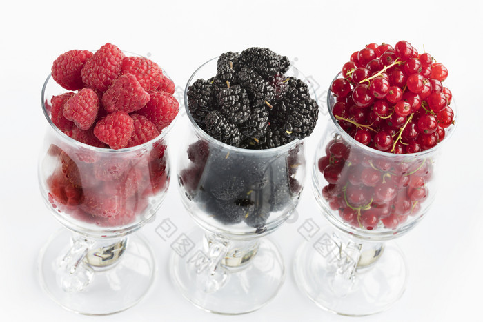 树莓大黑色的黑莓和红色的醋栗是倒成透明的玻璃杯为拿铁和站行光背景的图像高关键树莓大黑色的黑莓和红色的醋栗是位于清晰的玻璃光背景