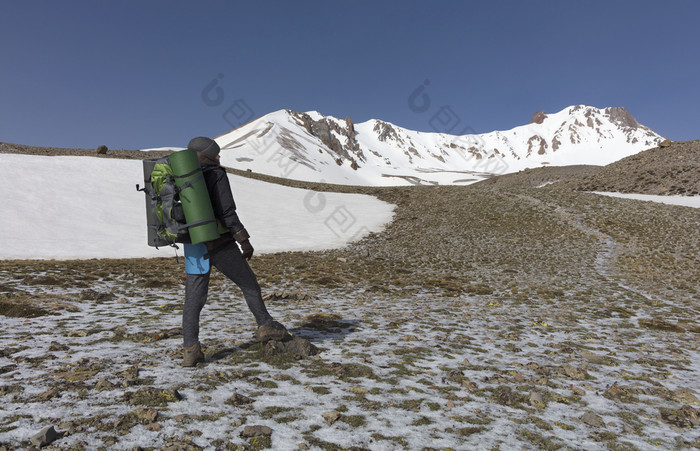 旅游女人与背包她的回来和跟踪坚持她的手去运动的白雪覆盖的山的旅游上升的山腰的白雪覆盖的峰会