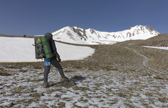 旅游女人与背包她的回来和跟踪坚持她的手去运动的白雪覆盖的山的旅游上升的山腰的白雪覆盖的峰会