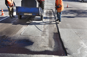 的路维护工人喷雾的沥青混合物到的清洗区域为更好的附着力的新沥青部分修复的沥青路的工人喷雾沥青的沥青表面