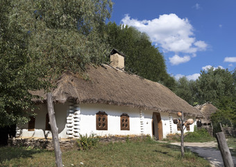 老传统的乌克兰农村房子与茅草屋顶和柳条栅栏的花园对蓝色的天空与白色<strong>云</strong>老传统的乌克兰农村房子与茅草屋顶和柳条栅栏的花园