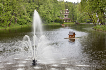 风景如画的春天公园与喷泉的中间大和宽池塘和两个浮动房子为鸭子对的背景舒适的咖啡馆喷泉的中间的池塘和浮动鸭房子的风景如画的公园