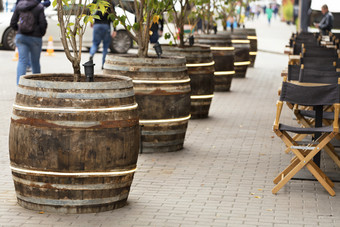 大木老酒桶与生锈的金属篮球服务锅为年轻的树和站沿着街咖啡馆大木老桶站沿着的街咖啡馆