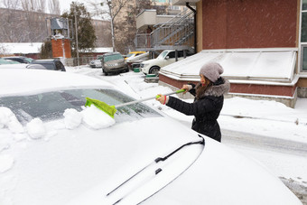 年轻的美丽的女人黑色的外套清洗的雪与折叠绿色长刷从的表面她的车年轻的女人清洗雪从的表面她的车