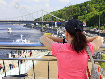 年轻的女人看<strong>起来</strong>的路堤的第聂伯河河基辅乌克兰夫人旅行者明亮的粉红色的t恤站的观察甲板和看<strong>起来</strong>对的桥年轻的女人看<strong>起来</strong>的路堤桥和河