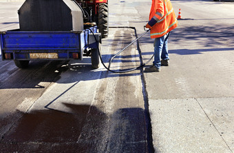 的路维护工人喷雾的沥青混合物到的清洗区域为更好的附着力的新沥青部分修复的沥青路的工人喷雾沥青的沥青表面