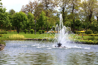 美丽的喷泉的中间春天池塘对的背景风景如画的城市公园绿色草地和开花栗子美丽的喷泉的中间春天池塘对的背景风景如画的城市公园