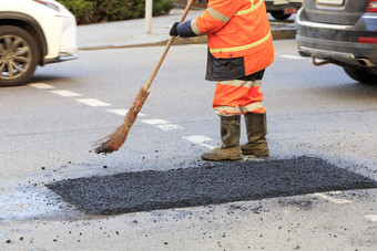 的路工人清洁工与圆锥花序走了与新鲜的沥青的修理拉伸路路建设路工人收集新鲜的沥青与圆锥花序的部分的路被修理