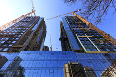 片段的外观现代建筑下建设使玻璃和混凝土反映了的玻璃墙相邻建筑塔建设起重机指出向上的玻璃外观反射的蓝色的天空和起重机附近现代混凝土建筑下建设