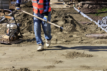 工人对齐的基金会与沙子和铲为铺设铺平道路板的背景汽油框架和准备区域为工作铺设瓷砖的人行道上工人携带建设铲沙子水平的基金会