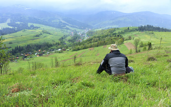 孤独的旅行者坐在的草前山和看起来的风景如画的景观的喀尔巴阡山脉的山和的村的谷笼罩雾旅行者rsquo视图的风景如画的景观的喀尔巴阡山脉的山和的村的谷笼罩雾