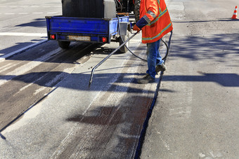 服务路维护工人喷雾的沥青混合物到的清洗区域为更好的附着力的新沥青工人维修部分的沥青路喷涂沥青的沥青表面