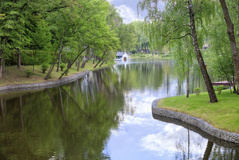 森林池塘与喷泉美丽的风景如画的夏天公园位于在各种各样的落叶树框架的银行连接鹅卵石和绿色草装饰池塘和浮动鸭房子与喷泉美丽的风景如画的夏天公园