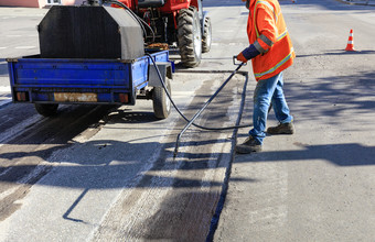 服务路维护工人喷雾的沥青混合物到的清洗区域为更好的附着力的新沥青工人维修部分的沥青路喷涂沥青的沥青表面