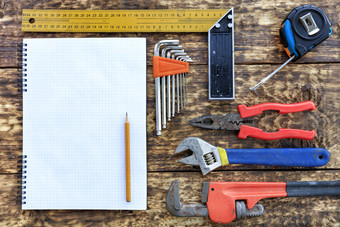 老手工具钳磁带测量可调扳手集十六进制键表明空笔记本与铅笔对的背景老木表格各种各样的手工具和空白记事本与铅笔老木背景