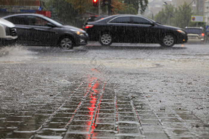 暴雨雨的路和的人行道上倒通过汽车照亮红色的交通光重雨的人行道上和沥青路照亮红色的交通光