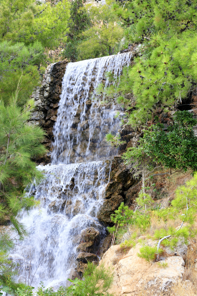 大瀑布从春天氡水流下来大巨石的脚的山在的绿色地中海松树和棕榈树的公园洛特拉基希腊垂直图像大瀑布与氡水在的巨石的脚的山洛特拉基希腊垂直图像