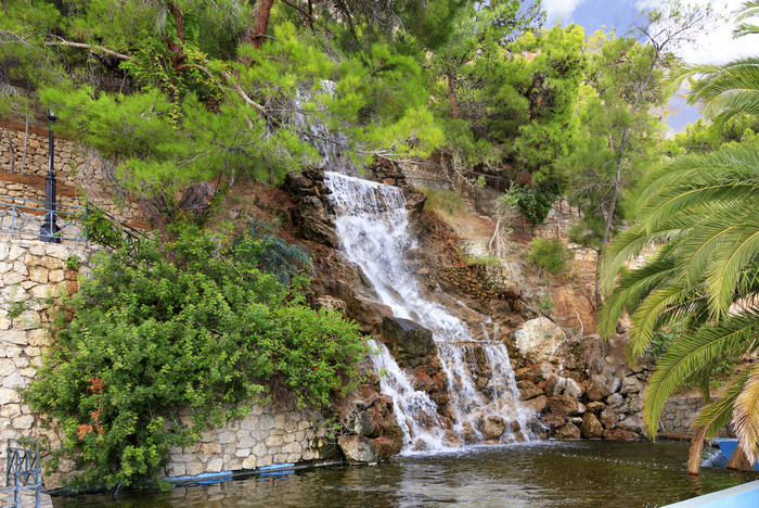 大瀑布从春天氡水流下来大巨石的脚的山在的绿色地中海松树和棕榈树的公园洛特拉基希腊大瀑布与氡水在巨石的脚山洛特拉基希腊