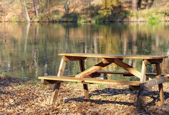 简单的木表格与野餐长椅的开放空气背景下降橡木叶子附近森林湖温暖的秋天一天模糊与复制空间木表格与野餐长椅的开放空气的背景下降橡木叶子附近森林湖