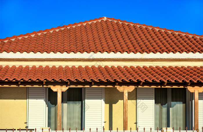 倾斜的光棕色（的）粘土瓷砖屋顶农村传统的单层房子南部希腊覆盖与棕色（的）瓷砖对蓝色的天空倾斜的光棕色（的）粘土平铺的屋顶农村传统的单层房子南部希腊点它的峰蓝色的天空