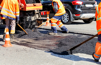 的集团路工人更新部分的路与新鲜的沥青使用铲子和水平修复的车道工作团队水平的新鲜的沥青与铲子修理区域路建设