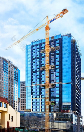 的建设现代住宅混凝<strong>土建</strong>筑与玻璃外观塔起重机使用的蓝色的天空反映了的窗户的建筑的玻璃外观反射的蓝色的天空和起重机附近现代混凝<strong>土建</strong>筑下建设