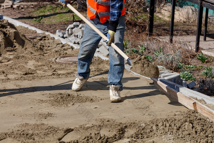 工人水平的基金会与沙子和铲下木水平为铺设铺平道路板对的背景的工作场所和准备为工作工人与铲穿沙子水平的基金会下的铺平道路板