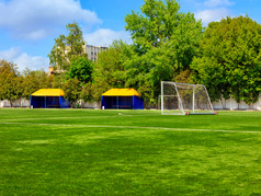 绿色草坪上足球场与盖茨网和帐篷为团队球员夏天一天对背景绿色树叶和略多云的蓝色的天空绿色草坪上足球场与盖茨和帐篷为团队球员