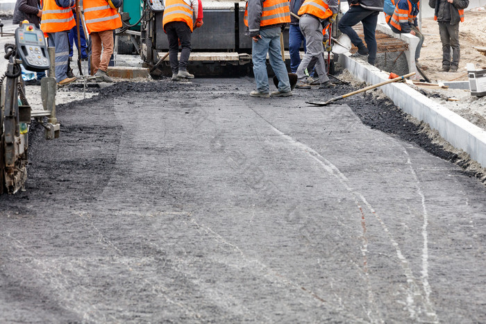 的工作集团路工人更新的拉伸路与新鲜的热沥青和轻抚修复的路表面的巷道复制空间工作集团路工人均匀分配的第一个层热沥青与铲子手动在的路部分被修理