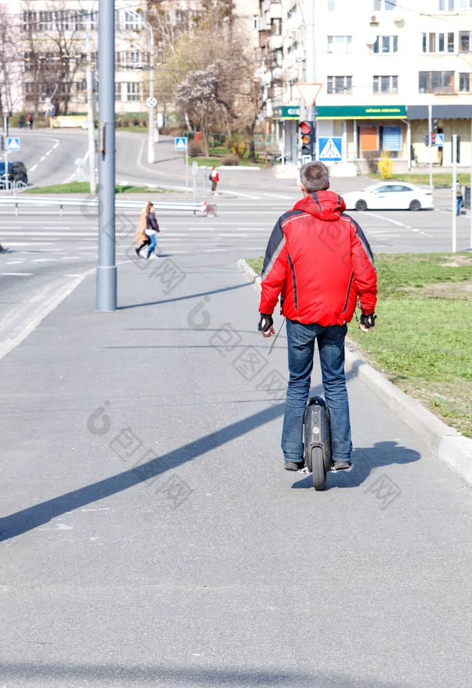男人。红色的夹克移动电单轮沿着的人行道上城市街现代概念自由运动年轻的男人。红色的夹克移动单轮的人行道上